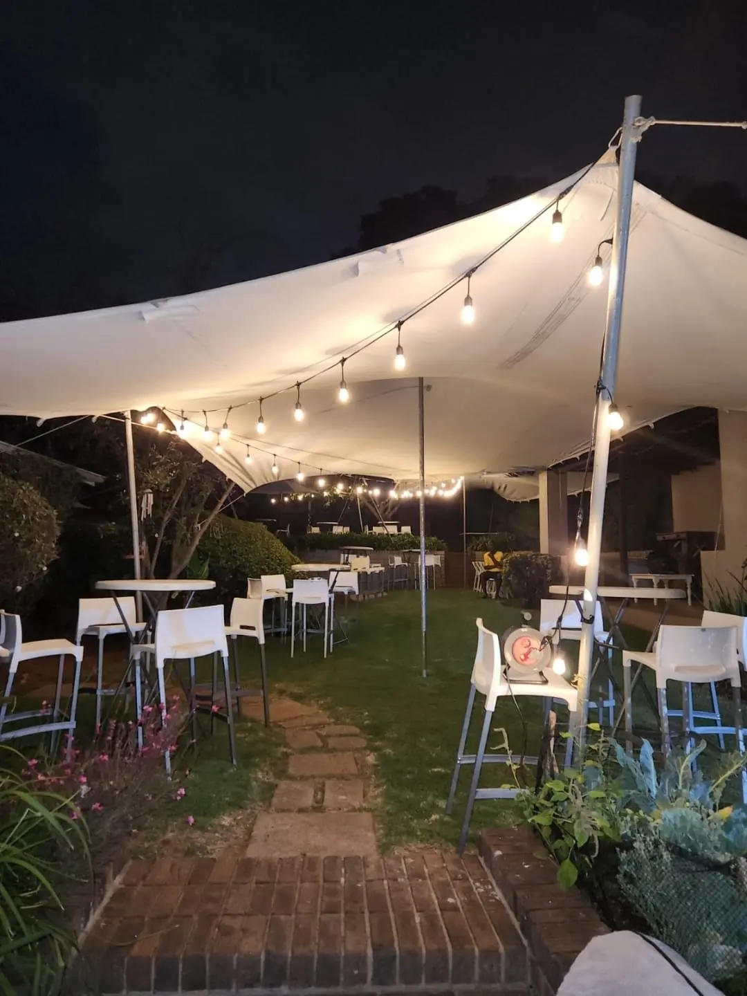 Cocktail tables and bar stools under a white stretch tent with warm festoon string lighting at night — evening cocktail and bar setup hire by Decorvent Hire