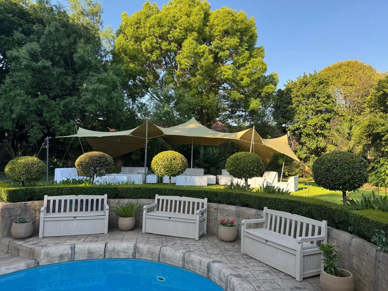 Golden stretch tent with white lounge furniture in garden poolside — stretch tent hire Johannesburg