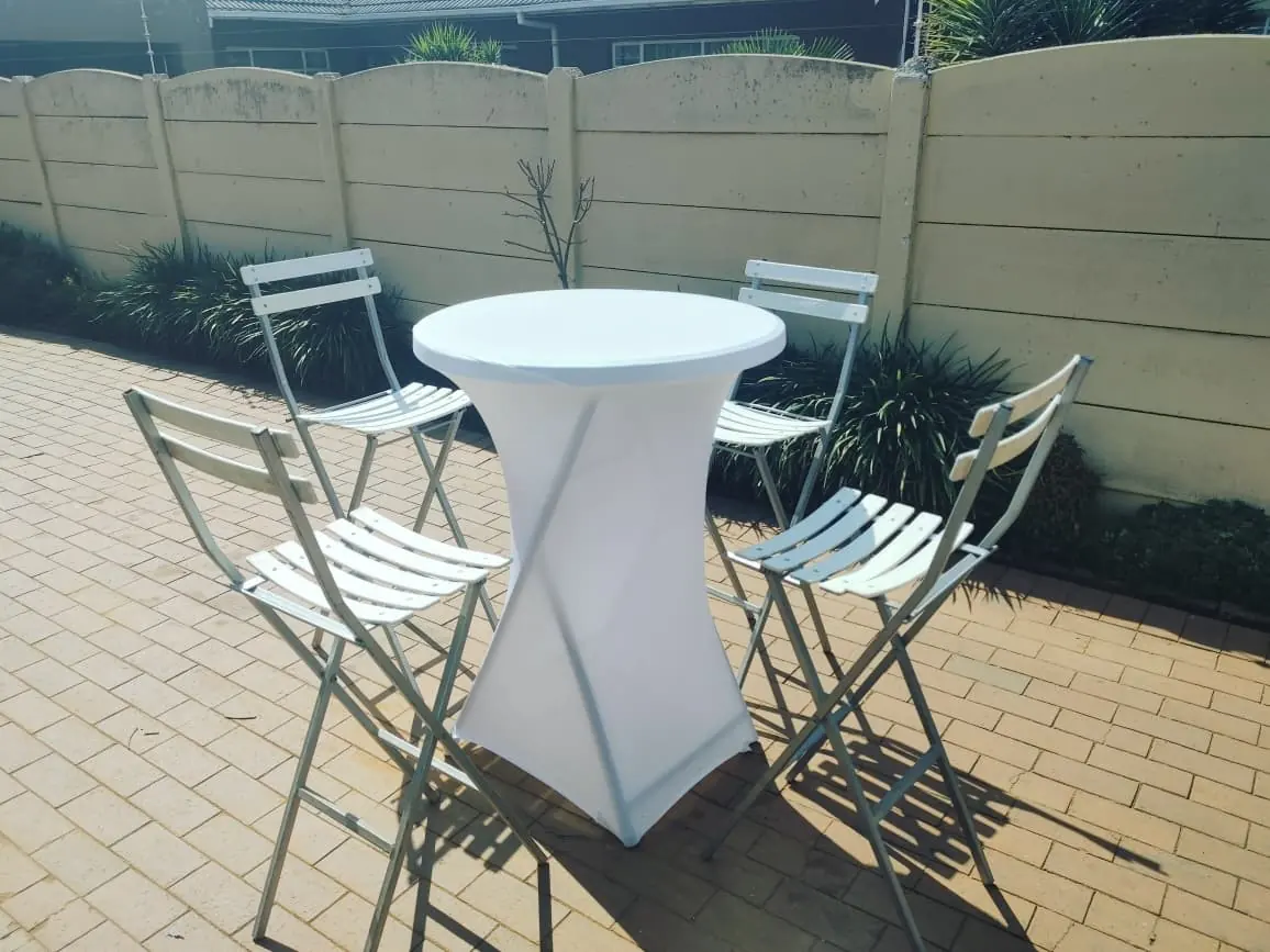 Round cocktail table with folding bar chairs on a paved patio