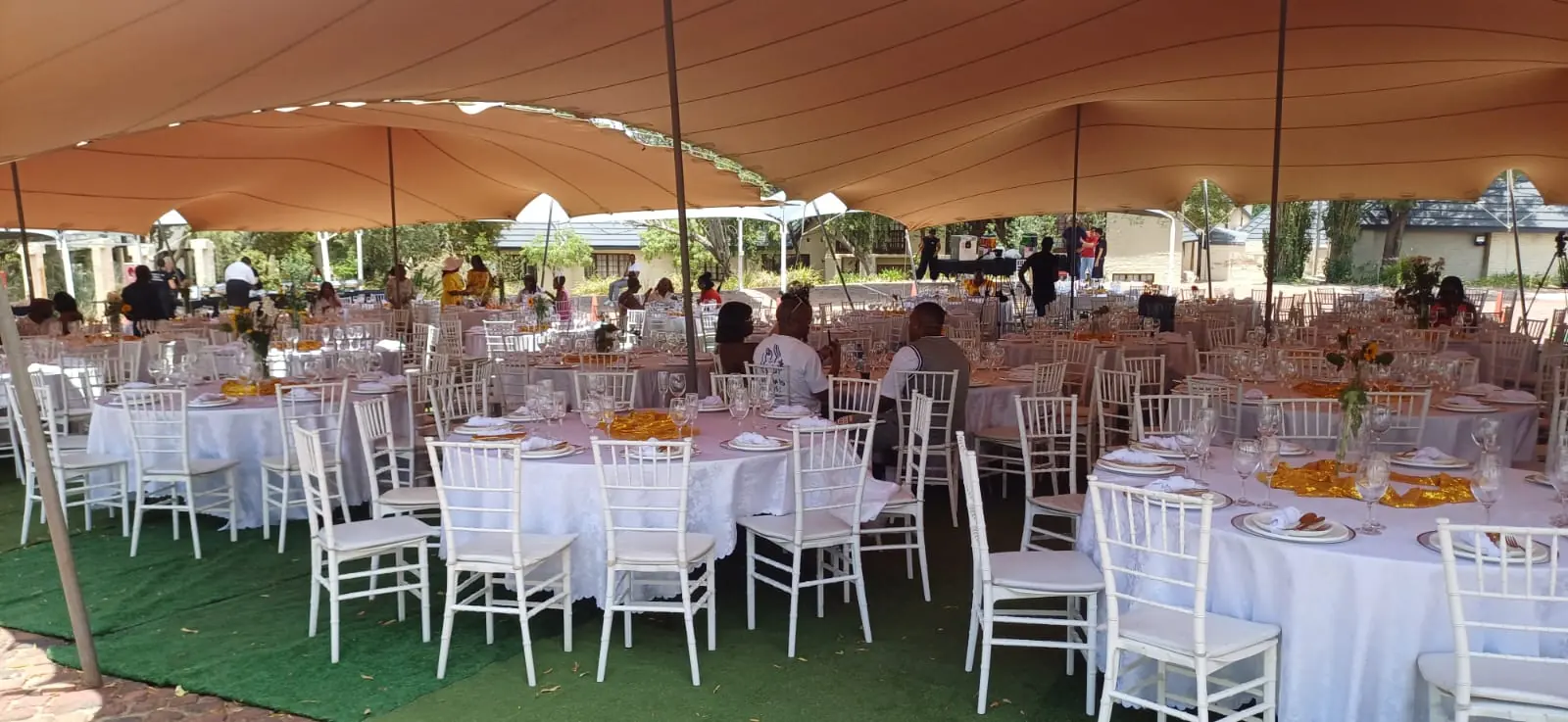 Round tables with Tiffany chairs dressed in white linen and gold runners under a stretch tent — wedding table and chair hire by Decorvent Hire Gauteng
