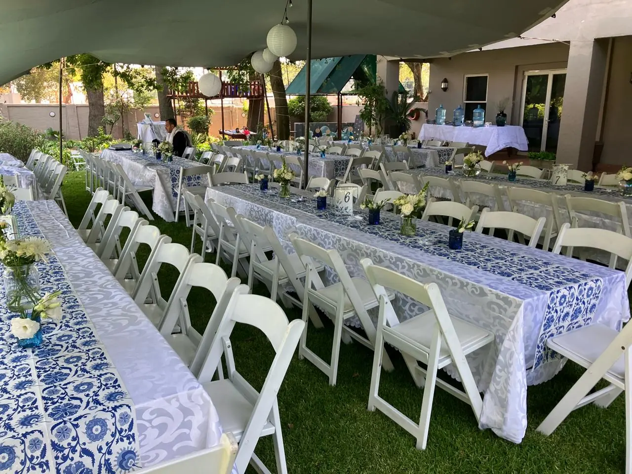 Tables and chairs set up under a stretch tent with white folding chairs, decorated trestle tables, floral centrepieces and table runners — wedding setup by Decorvent Hire Gauteng