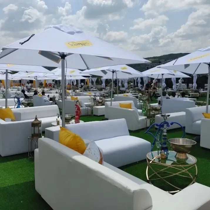 White 2.7m patio umbrellas shading white lounge couches with yellow scatter cushions on artificial grass at an outdoor party — garden umbrella hire Gauteng