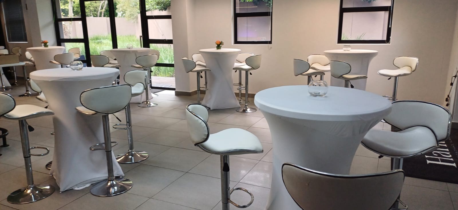 White spandex cocktail tables with cushioned chrome bar stools set up for a corporate cocktail function — cocktail and bar setup hire by Decorvent Hire Gauteng