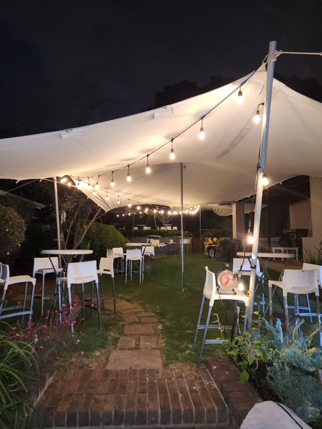 Cocktail tables and bar stools under a white stretch tent with warm festoon string lighting at night — evening cocktail and bar setup hire by Decorvent Hire