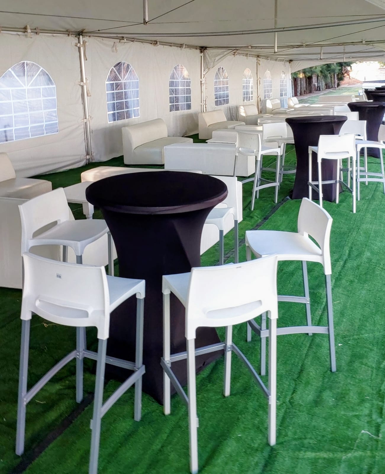 Cocktail tables with black spandex covers and white bar stools set up under a stretch tent for a daytime event — cocktail and bar setup hire by Decorvent Hire Gauteng